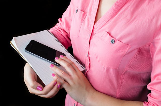 Une étudiante avec un carnet et un mobile.
